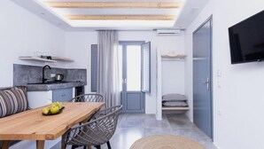 Eine kompakte Küche mit Holzbalkendecke, eine Essecke mit Tisch und Stühlen sowie ein an der Wand befestigter Fernseher.