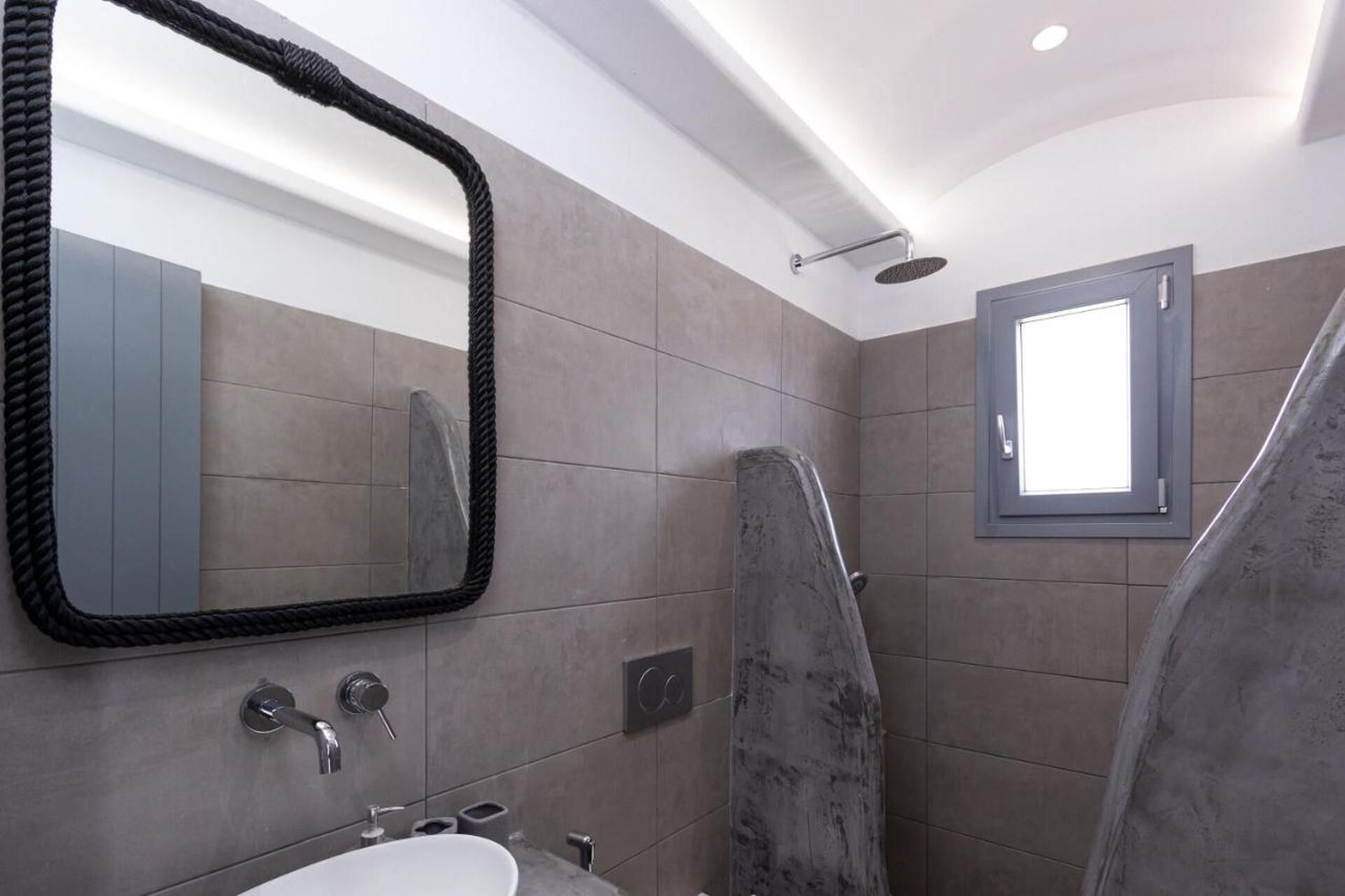 Une salle de bain moderne avec un grand miroir, un espace douche et une petite fenêtre.