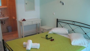 A bedroom with a bed, a bedside table, a small desk, and a bathroom visible in the background. - Verykokkos Pension 2 (Naxos)