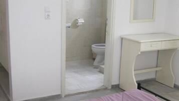 A bedroom with a bed, a bedside table, a bathroom with a toilet and shower, and a mirror on the wall.
