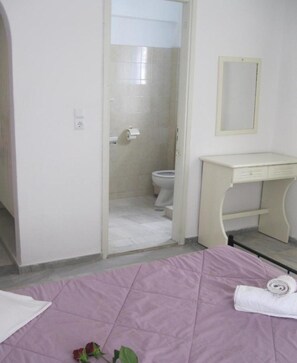 Un dormitorio con cama, mesita de noche, baño con inodoro y ducha, y un espejo en la pared.