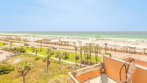 Un balcón con vista a una playa, palmeras y una carretera que lleva a la playa.