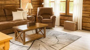 A log cabin interior with a brown leather sofa, a wooden coffee table, a brown armchair, and a wicker basket.