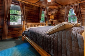 Un dormitorio de cabaña de madera con una cama, cabecera de madera y una ventana con cortinas.
