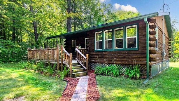 A log cabin with a wooden exterior, a porch, and a staircase leading to the entrance.