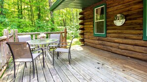 A wooden cabin with a deck, a round table, and chairs.
