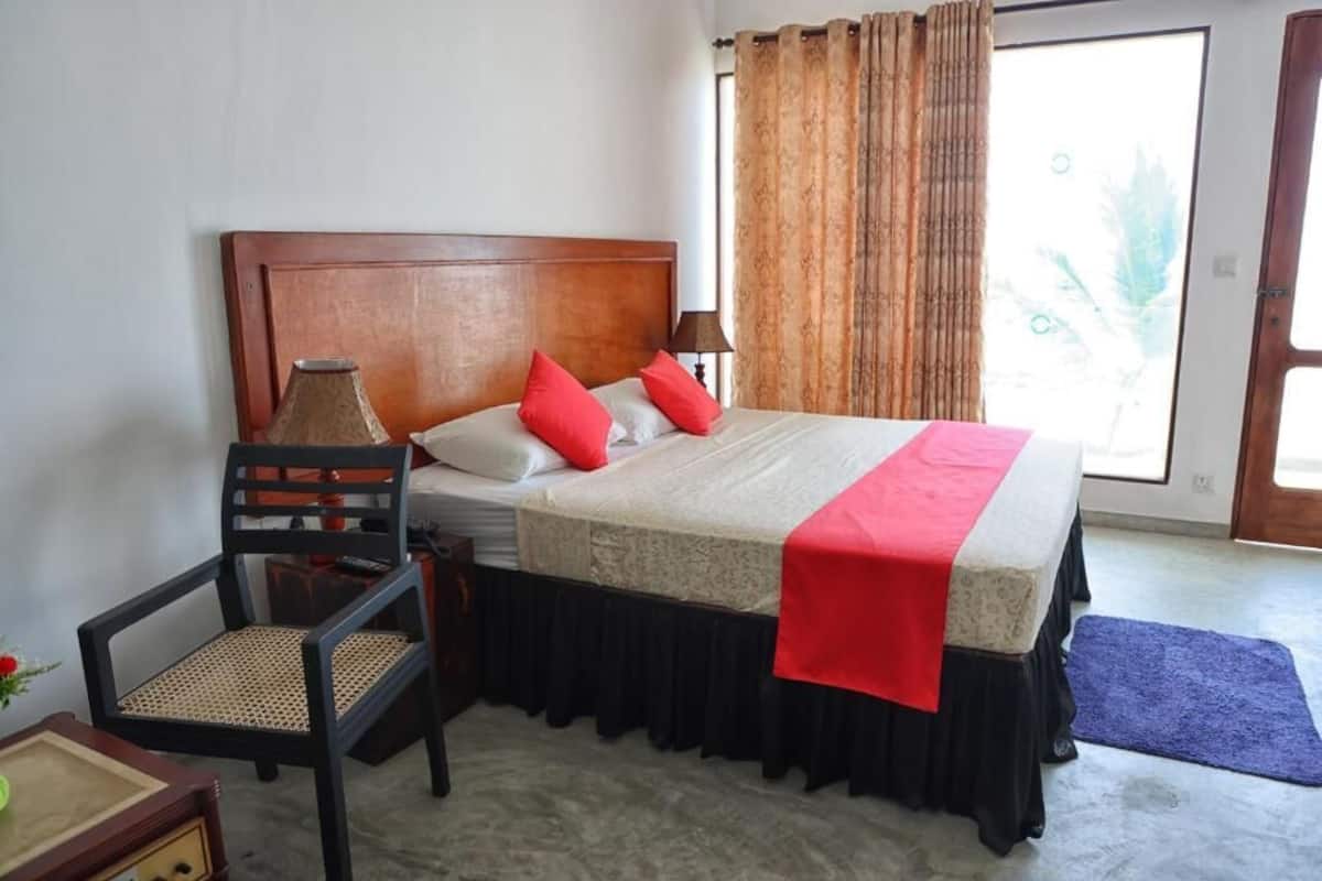 Une chambre d’hôtel avec une tête de lit en bois, un lit recouvert d’une courtepointe rouge et blanche, une chaise avec un siège en osier et une fenêtre avec des rideaux.