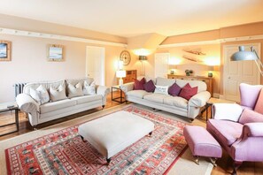 Ein Wohnzimmer mit zwei Sofas, einem rosa Sessel, einem gemusterten Teppich und einem Holztisch.