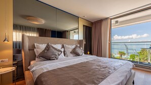 A modern hotel room with a large bed, a small side table, and a view of the sea.