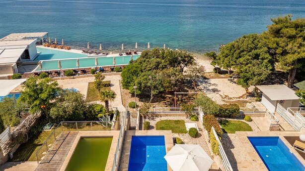 A resort with a large swimming pool, smaller pools, and a view of the sea.