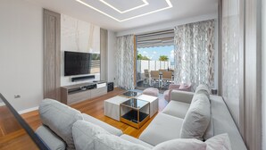 A modern living room with a flat-screen TV, a glass coffee table, and a sofa.
