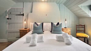 A bedroom with a large bed, two bedside tables, a chair, and a wooden door. - Lovely 2-bed Cottage in St Brides, Pembrokeshire (Haverfordwest)