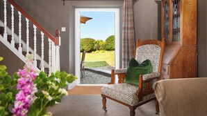 A room with a wooden staircase, a patterned armchair with a green pillow, and a wooden cabinet. - Lovely 2-bed Cottage in St Brides, Pembrokeshire (Haverfordwest)