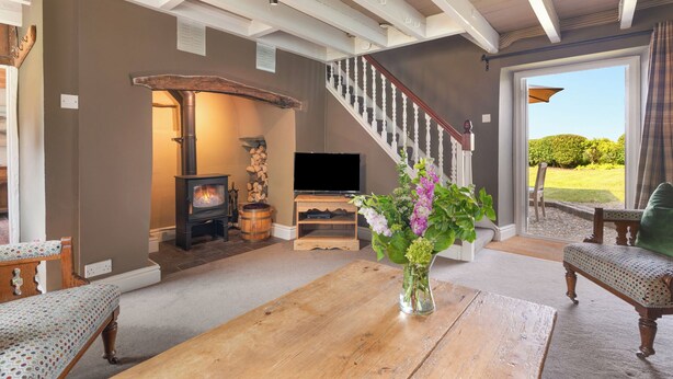 A spacious living room with a fireplace, a staircase, and a large window offering a view of the outdoors. - Lovely 2-bed Cottage in St Brides, Pembrokeshire (Haverfordwest)