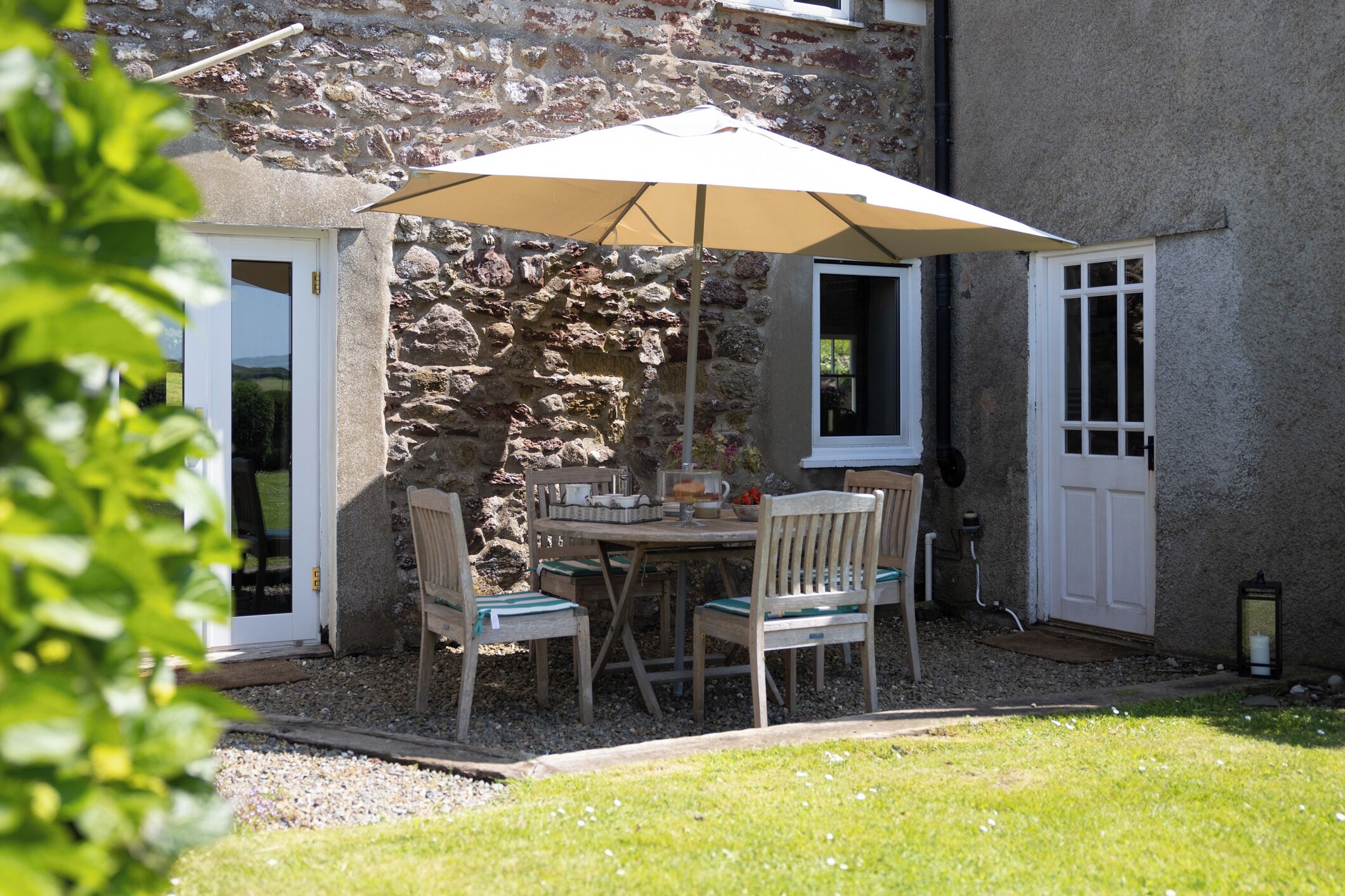 A stone building with a patio area featuring a table and chairs under a large umbrella.