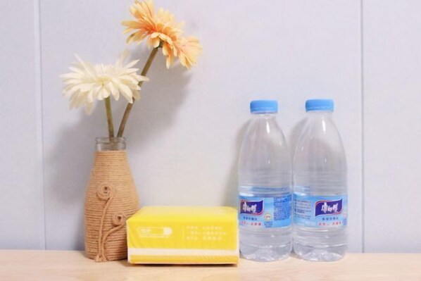 A wooden table with a vase of flowers, two water bottles, and a yellow sponge. - Lane Cottage B&B (Zhuhai)