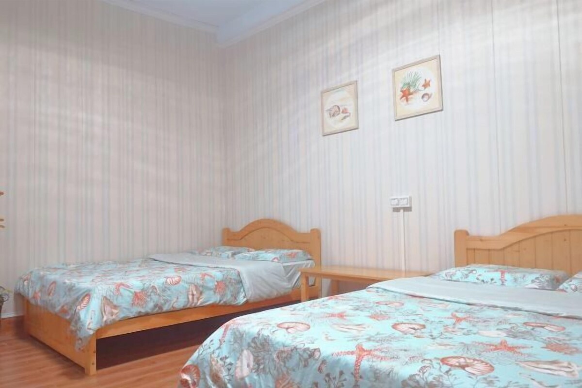 A room with two wooden beds, each with floral bedding, a wooden bench, and a wall-mounted light switch.