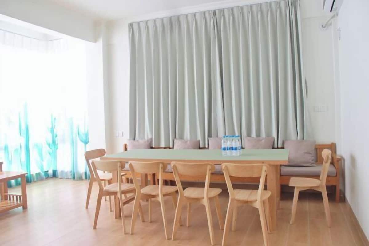 A dining area with a wooden table and chairs, a sofa, and a large window with curtains.