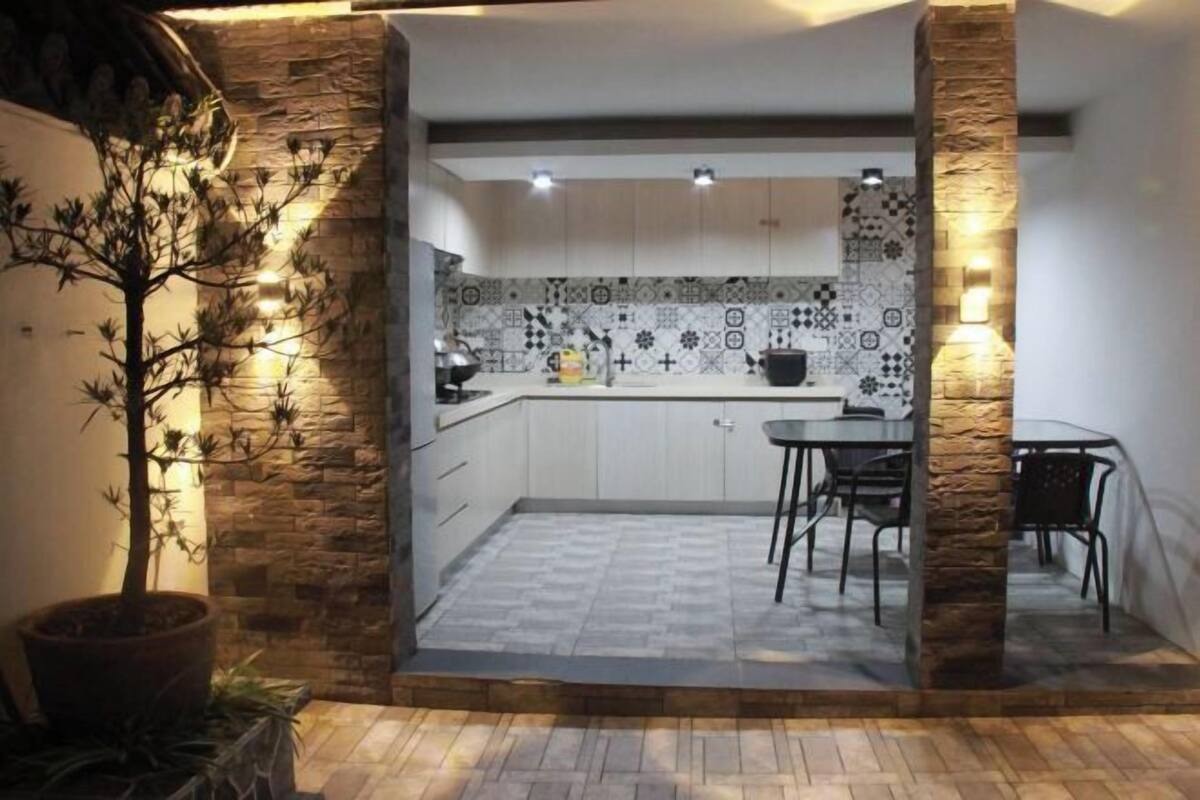 A compact kitchen with white cabinets, patterned backsplash, and a dining area with a table and chairs.