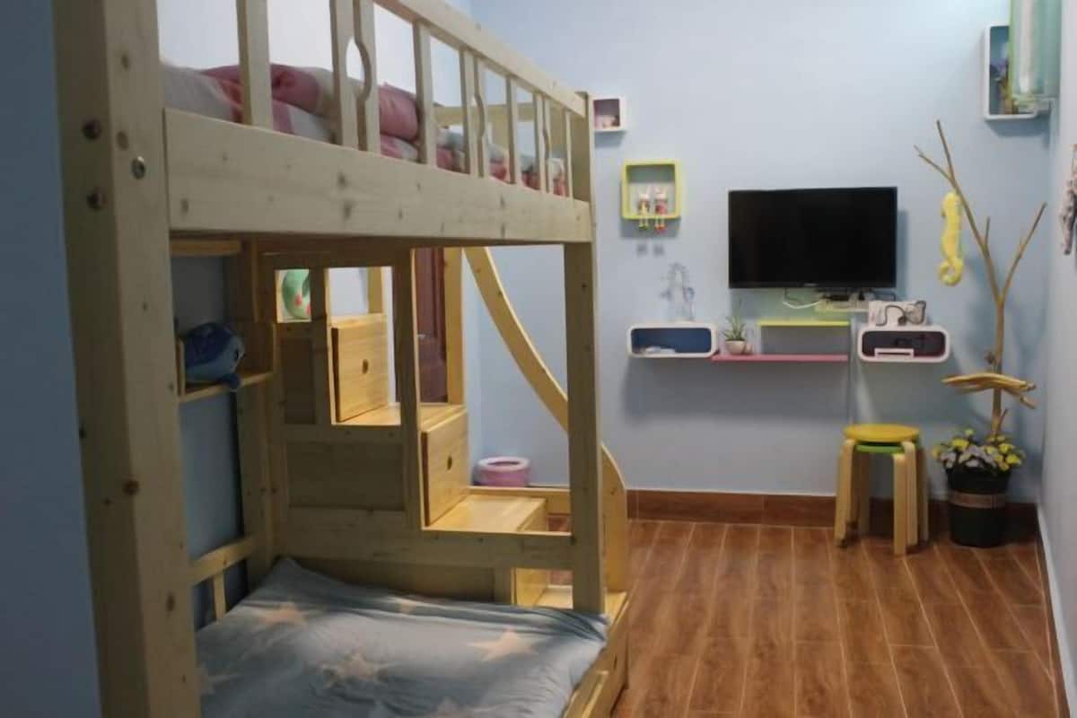 A bunk bed room with a TV, small stool, and a plant.