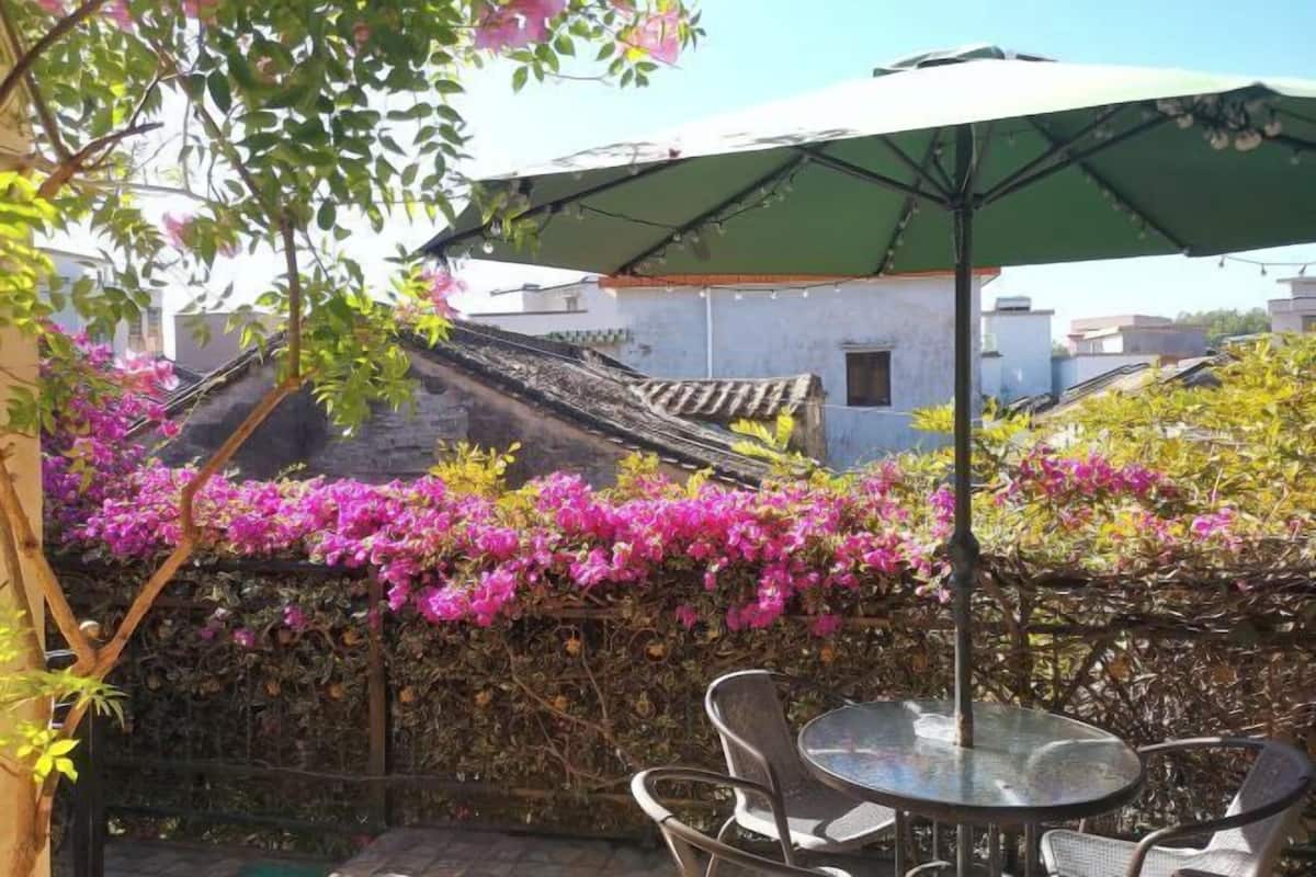 An outdoor patio with a round table and chairs, a green umbrella, and flowering vines.