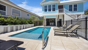 A pool area with a clear blue pool, lounge chairs, and a two-story house with a balcony. - Sip by the Pool - One bedroom, Pool, Beach Access (Pawleys Island)