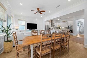 A spacious dining area with a wooden table and chairs, a ceiling fan, and a kitchen in the background. - Prominence Next to The Big Chill! 6-Seater LSV/Golf Cart, 4 Bikes, GULF VIEWS! (Alys Beach)