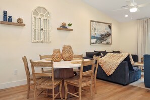 A dining area with a round wooden table and chairs, a white-framed window, and a ceiling fan. - Sunset CSB K66: Beach & Pool Views 4 Master Suites (Cape San Blas)
