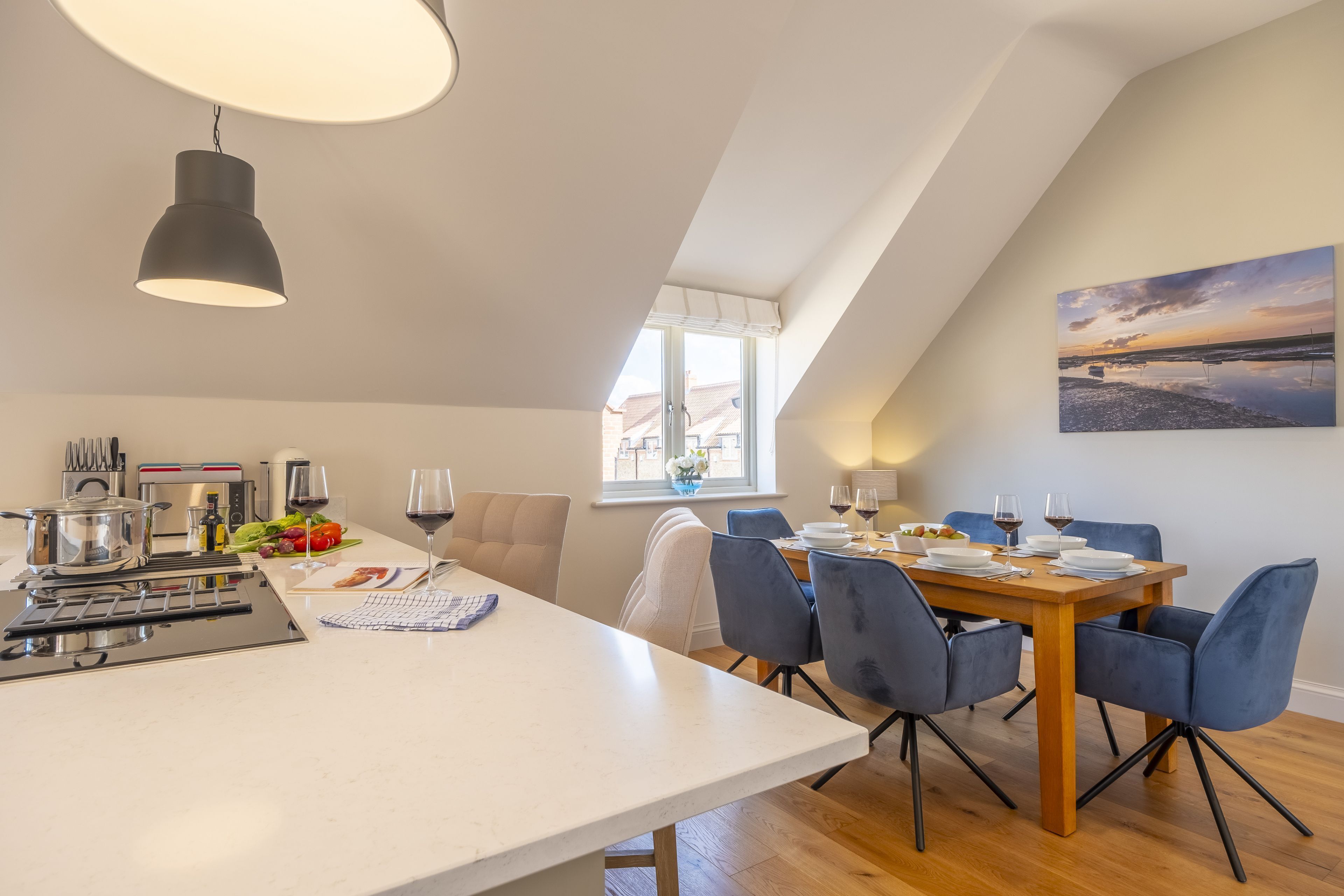 A modern kitchen with a dining area, featuring a large island, a built-in oven, and a view of the outside.