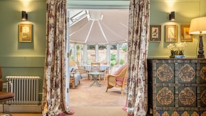 A conservatory with wicker furniture, a radiator, and framed artwork on the walls.