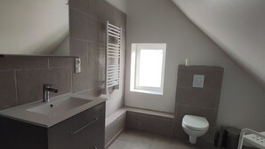Un baño pequeño y moderno con lavamanos, espejo, inodoro y ventana.