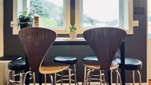 Comedor con una mesa y cuatro sillas, lámpara colgante y ventana con vista a follaje.