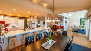 A spacious kitchen with a central island, a dining area with a large wooden table, and a living area with a sofa and a colorful coffee table. - 25%Off Sept 10-13 Amazing Location, Views, Hot Tub (Ventura)