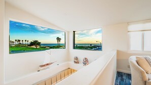 A modern room with a large window overlooking a beach, a small sailboat model, and a pair of owl-shaped slippers on the windowsill. - 25%Off Sept 10-13 Amazing Location, Views, Hot Tub (Ventura)
