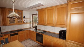 A kitchen with wooden cabinets, a dishwasher, a stove, and a coffee maker. - Mitten im Thüringer Wald, Ferienhaus für die Ganze Familie (Steinbach-Hallenberg)