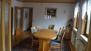 A dining area with a wooden table and chairs, a patterned rug, a painting on the wall, and a radiator near the window. - Mitten im Thüringer Wald, Ferienhaus für die Ganze Familie (Steinbach-Hallenberg)