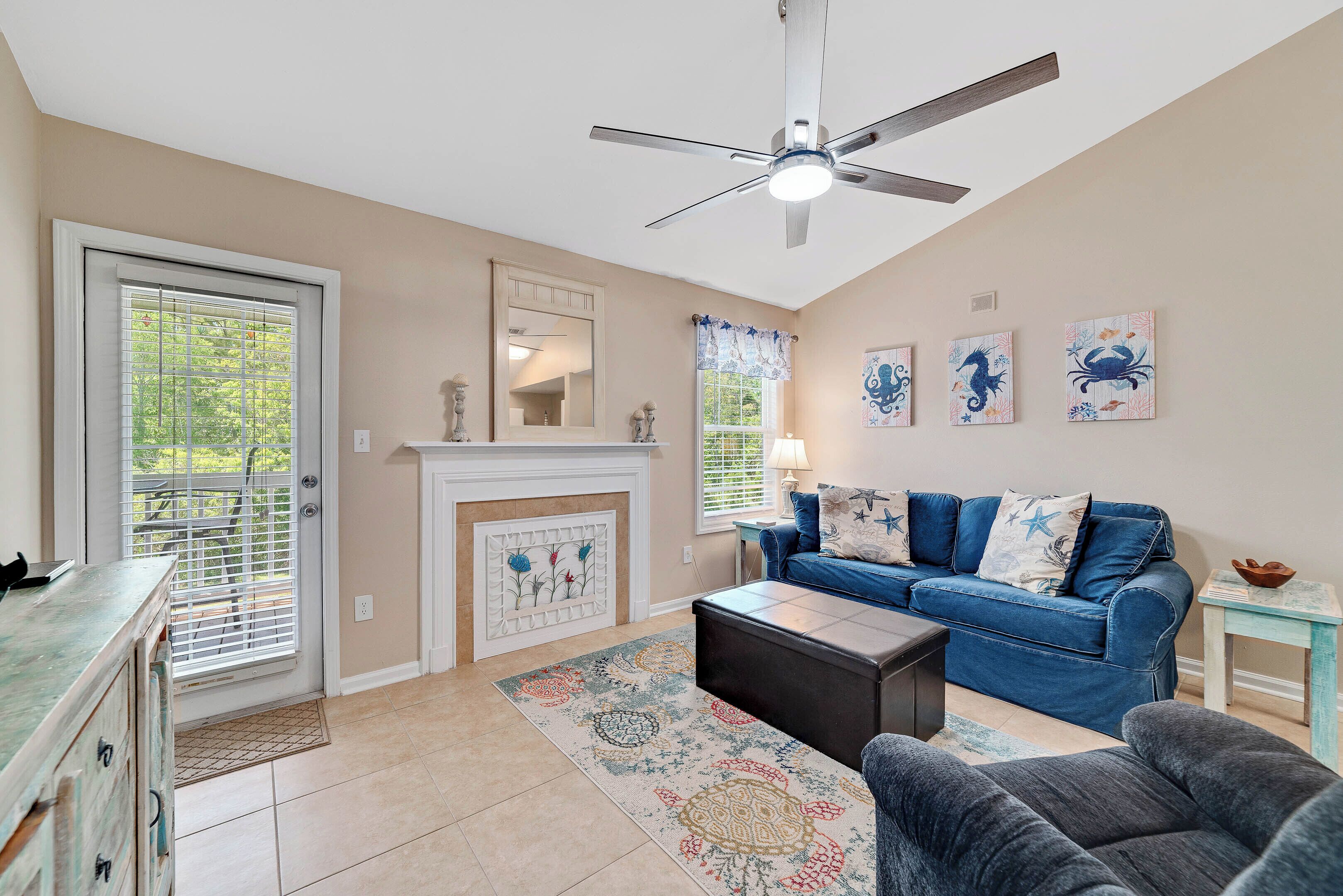 A living room with a fireplace, a ceiling fan, a blue sofa, and artwork on the wall.