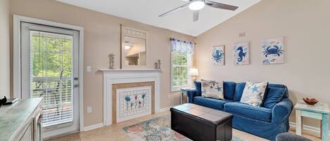 A living room with a fireplace, a ceiling fan, a blue sofa, and artwork on the wall.