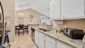 A kitchen with white cabinets, a granite countertop, a toaster, and a dining area with chairs and a table.