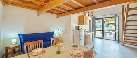 Un área de comedor con techo de madera, un sofá azul, una mesa de comedor con platos y cubiertos, y una cocina visible a través de una puerta abierta.
