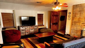 A living room with a television, wooden furniture, a red bean bag, and a stone wall. - One Acre Lakefront Home, Indian Hills Peninsula.  Pet friendly ! (Livingston)
