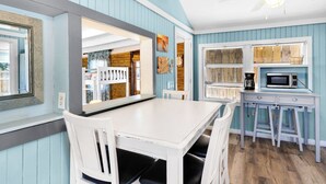 A dining area with a white table and chairs, a ceiling fan, and a kitchen area with a microwave and coffee maker.