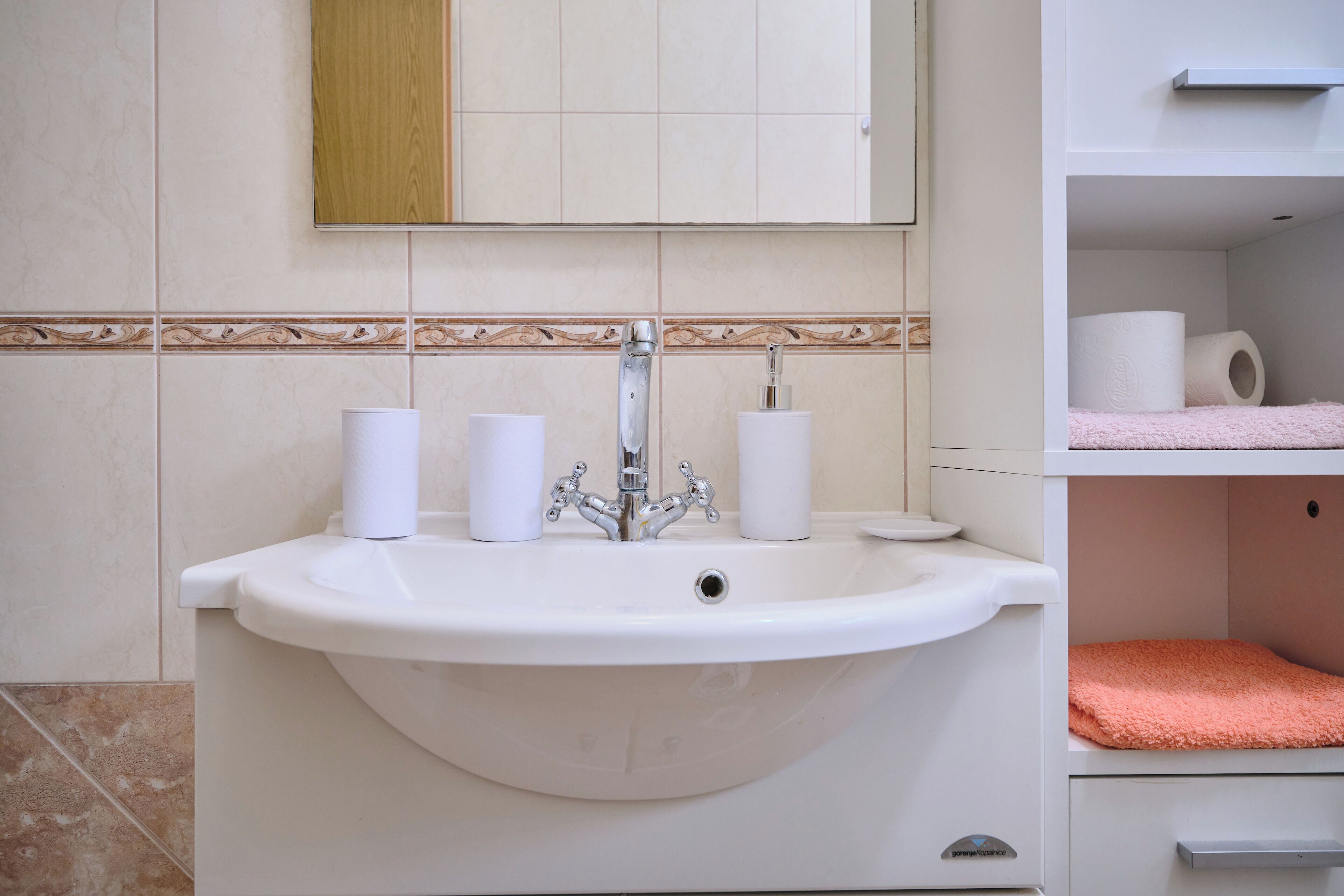 A bathroom with a white sink, two white toilet paper rolls, and a pink towel on a shelf.