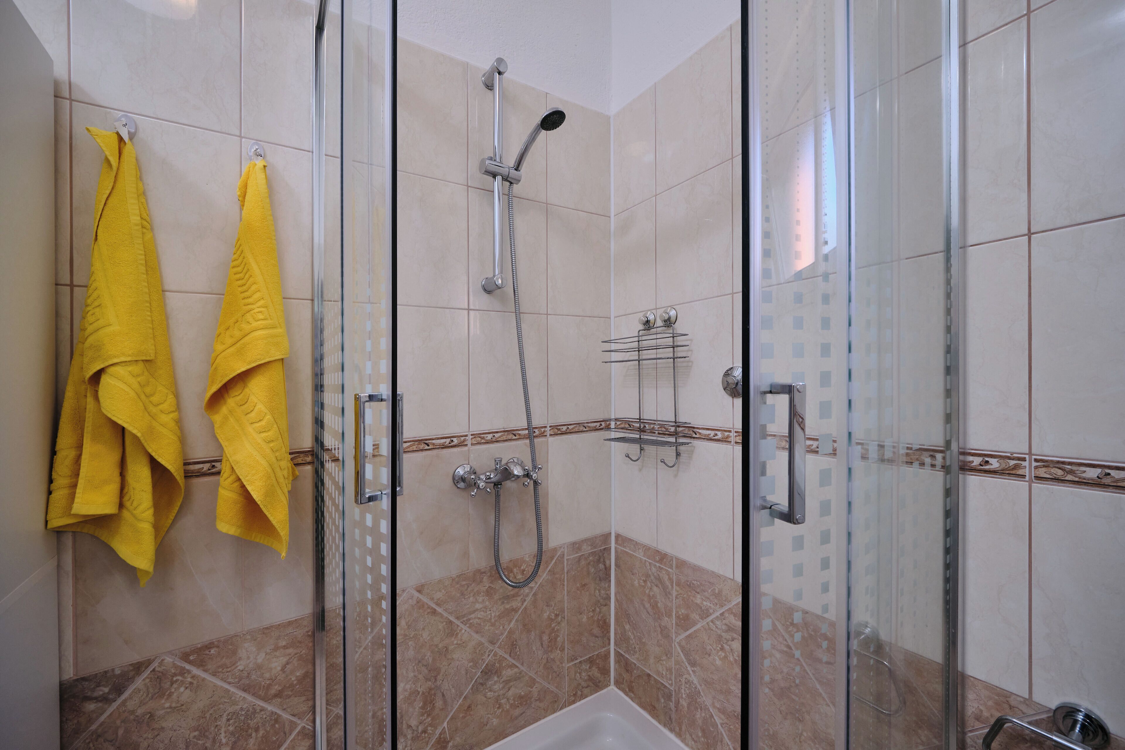 Cabina doccia con pareti in vetro, soffione a mano e rubinetto a parete.
