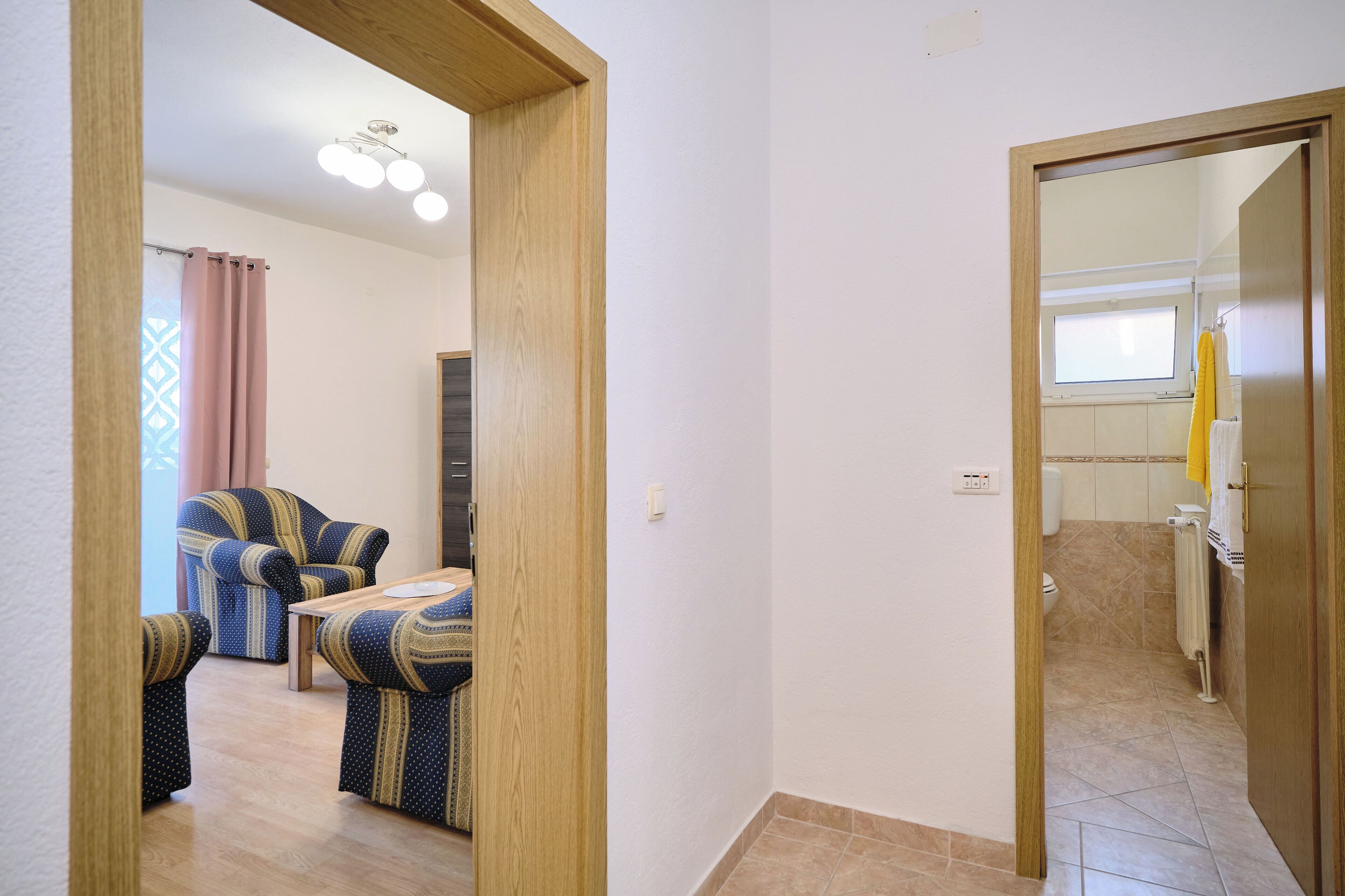 A room with a wooden floor, a sofa set, a small table, and a bathroom visible through an open door.