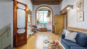 A spacious living room with a blue sofa, a coffee table with books and glasses, a wooden cabinet, and a large arched window with a view.