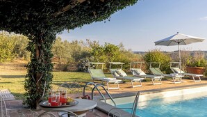 A poolside area with lounge chairs, a table with drinks, and a view of the countryside.