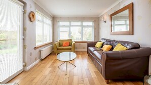 A living room with a brown leather sofa, a round glass table, a green armchair, and a large mirror on the wall. - Smugglers' Gait | Anstruther (Anstruther)