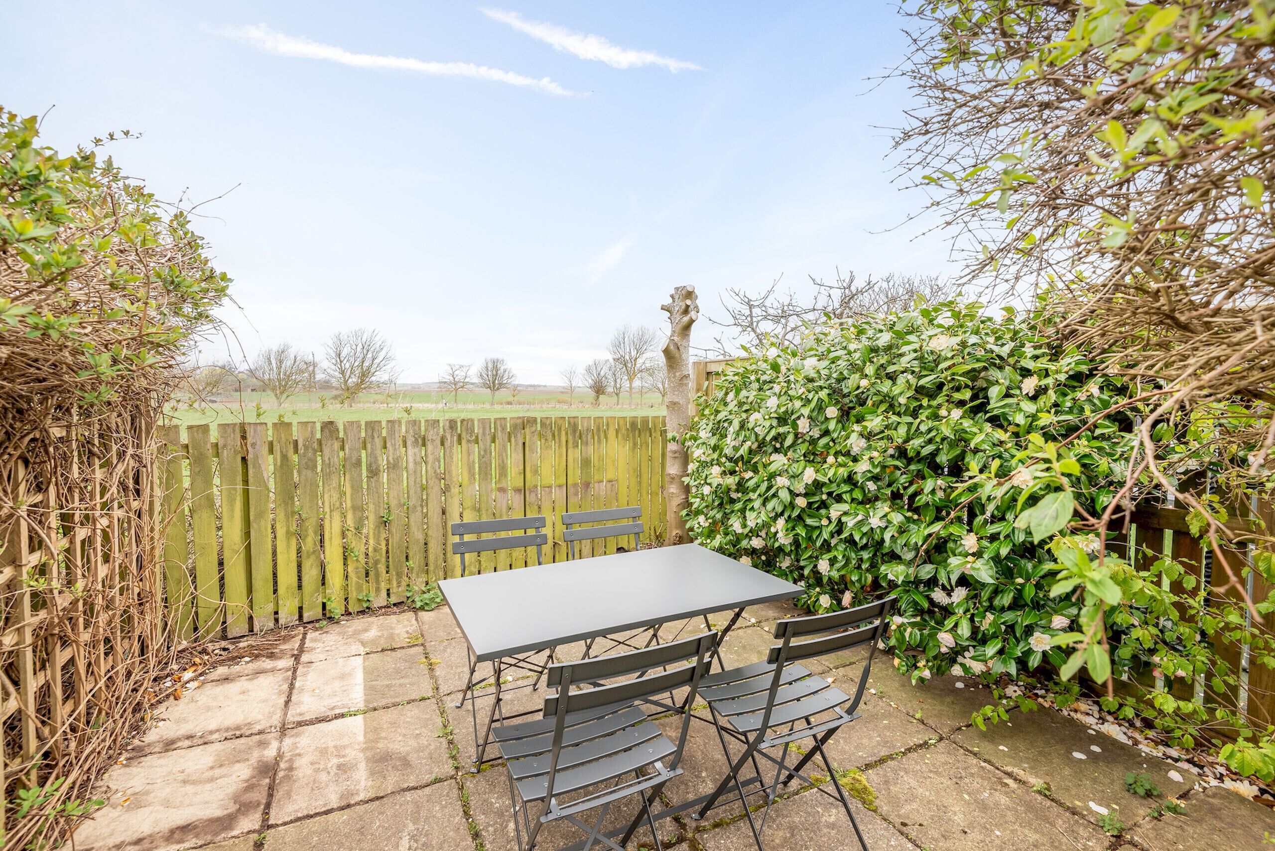 A patio with a table and chairs, surrounded by a wooden fence and greenery.