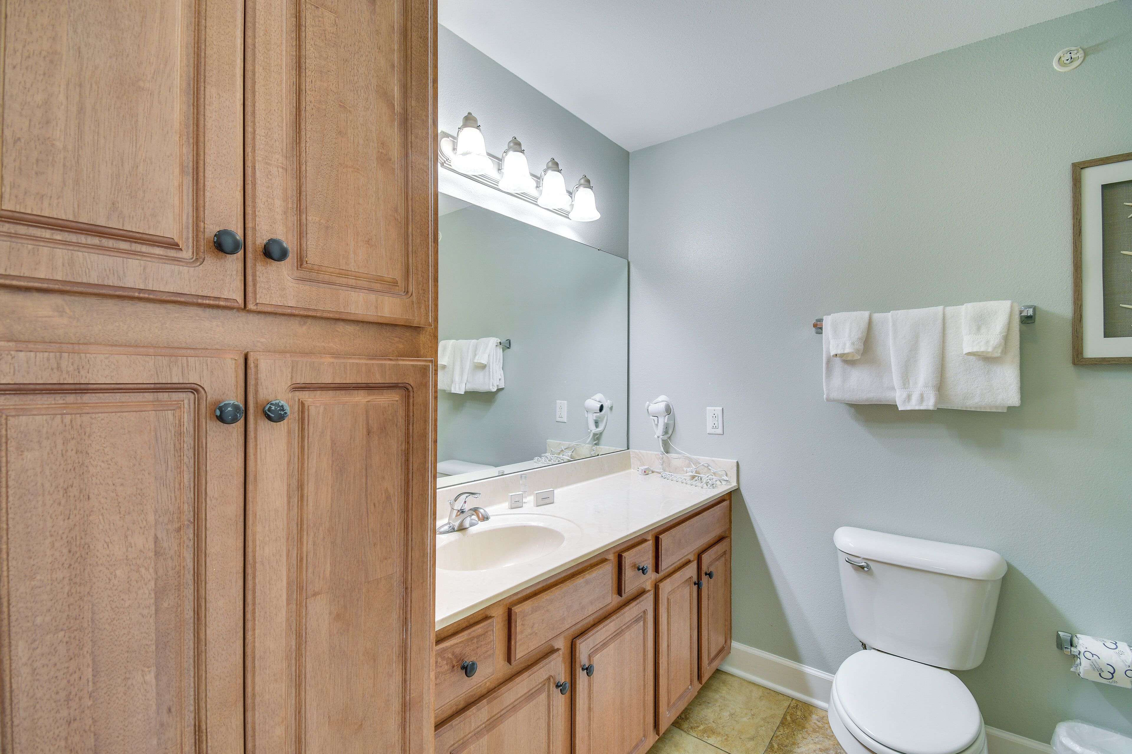 Un baño con muebles de madera, un lavabo, un inodoro y un espejo con iluminación.